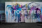 A mural of splattered multi color paint with the word Together placed above it
