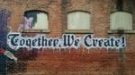 A brick wall spray painted with the words, Together we create!
